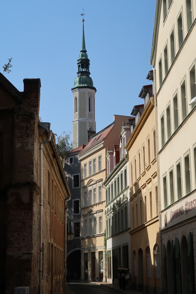 Looking down a narrow curving street with old pastel-coloured buildings either side and a point tower in the background
